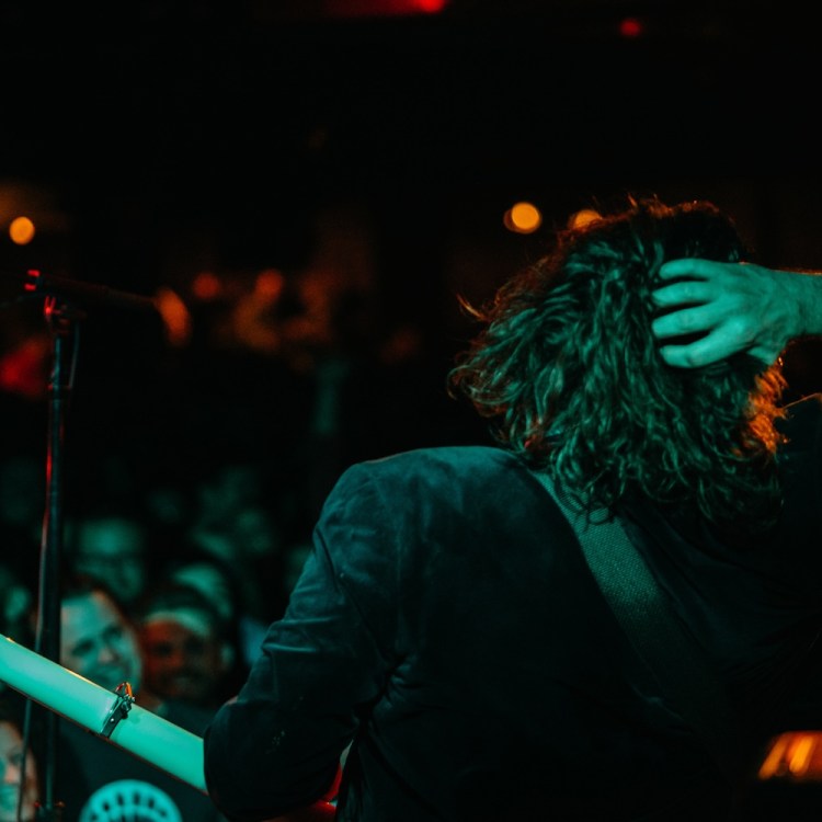 musician with guitar, hand on back of head, crown in distance, green light on him