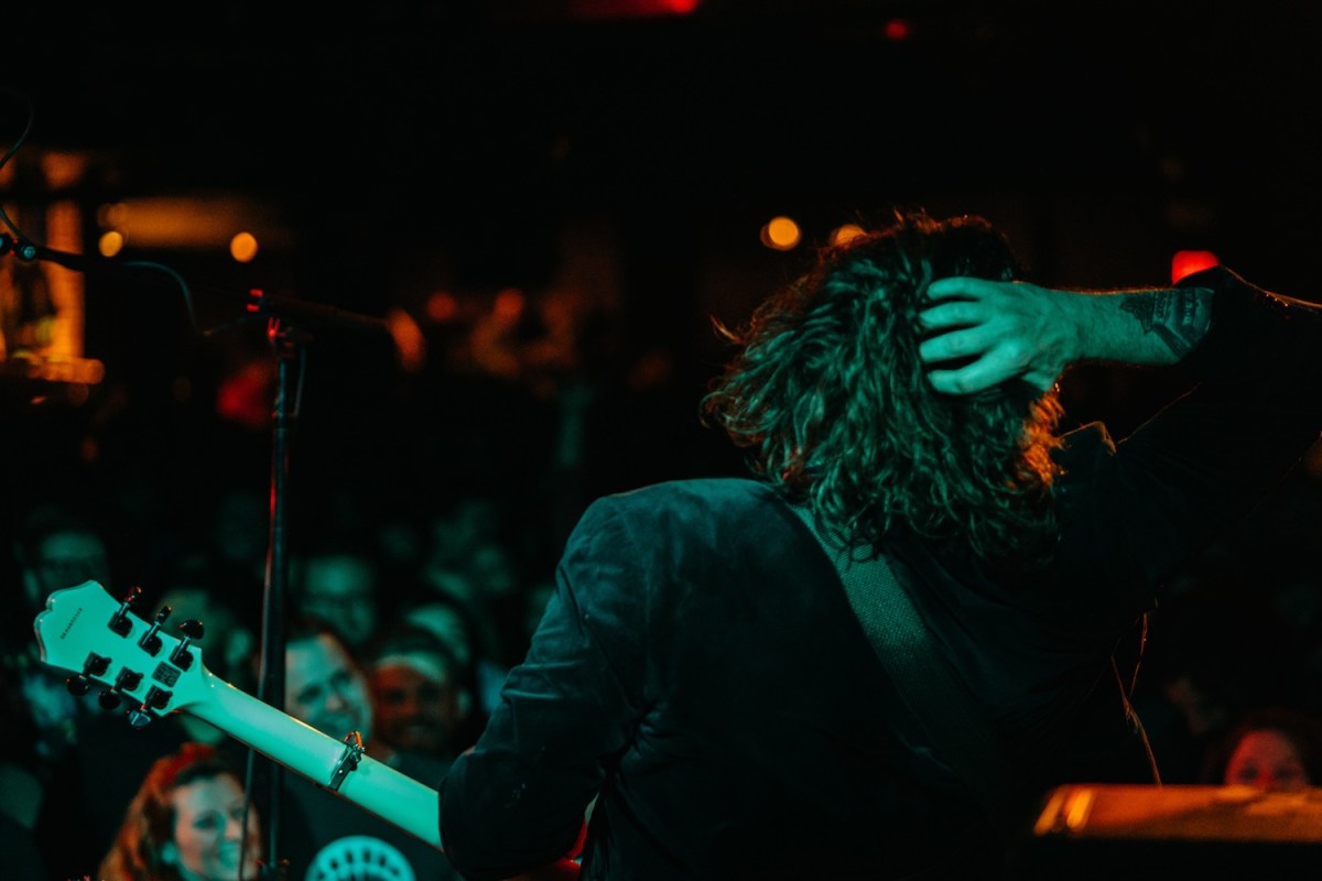 musician with guitar, hand on back of head, crown in distance, green light on him