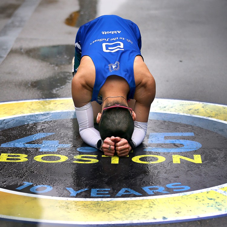 A man holds his head in his hands after completing the Boston Marathon.