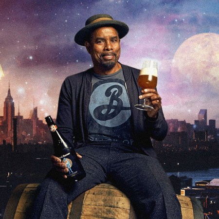 Garrett Oliver of Brooklyn Brewery holds a glass of beer while seated on a cask