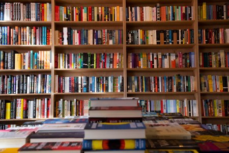 Books in a bookshelf behind a table of stacked books.