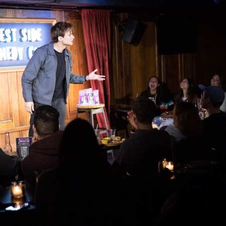 Man talking on a stage under a spotlight to a crowd of people, one of the places to see comedy in New York