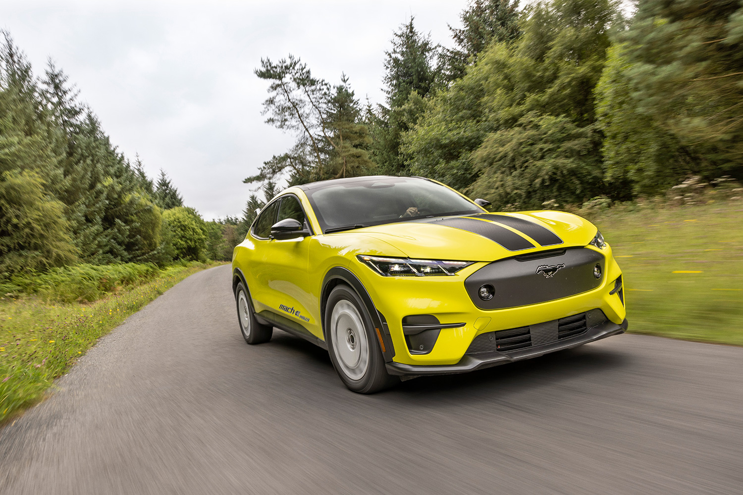 The Mustang Mach-E Rally in an eye-catching Grabber Yellow color flying down the road