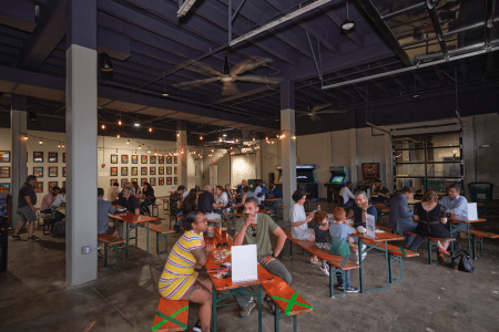 people sitting at tables in a seating area with neat lights and arcade games